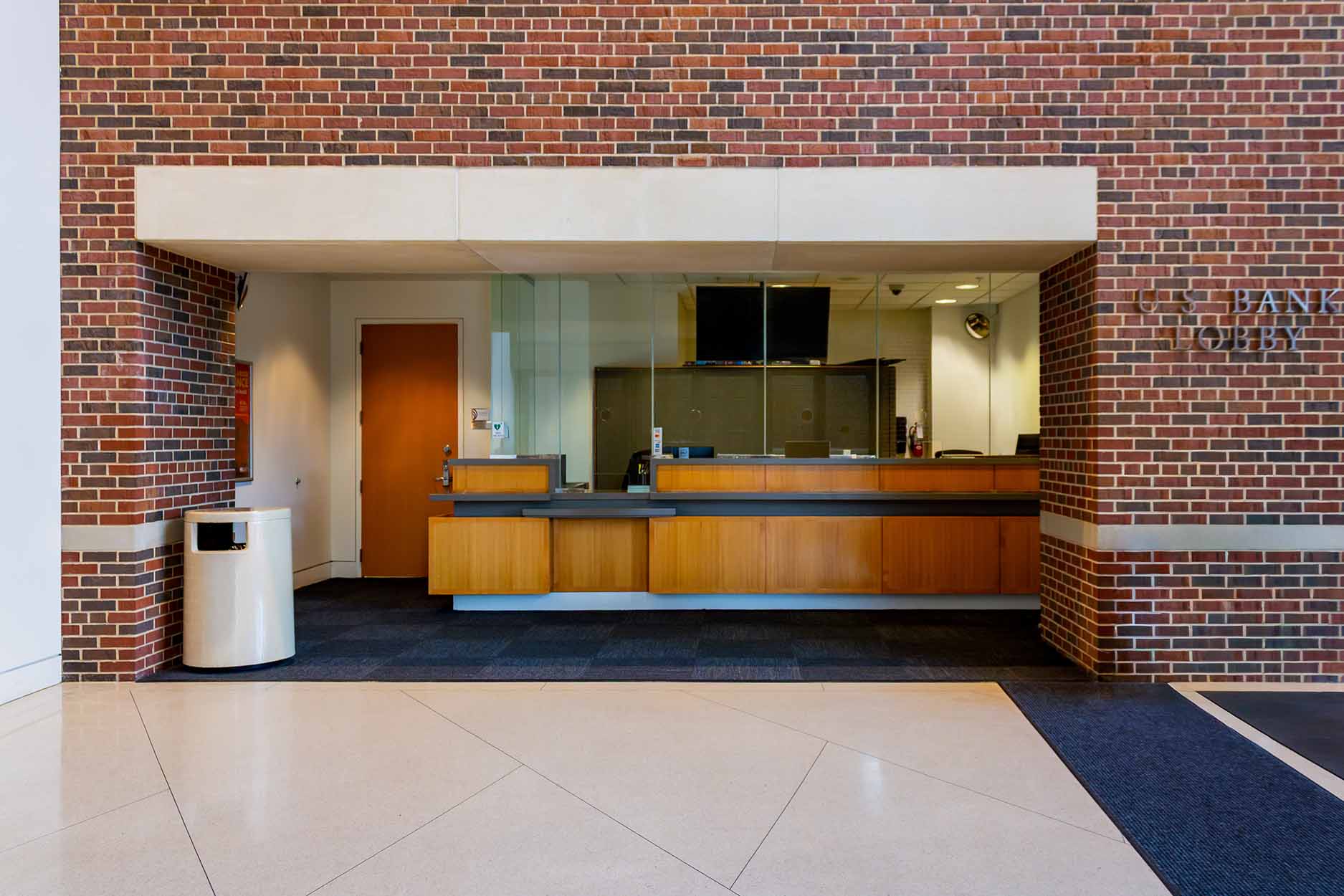 Bank lobby reception desk set into a brick wall, with a glass partition and a monitor behind the counter.